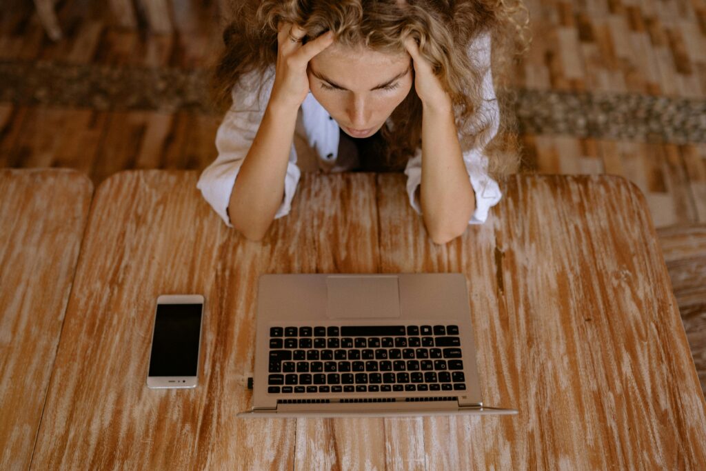 A woman looking stressed while working on a laptop from home, viewed from above.