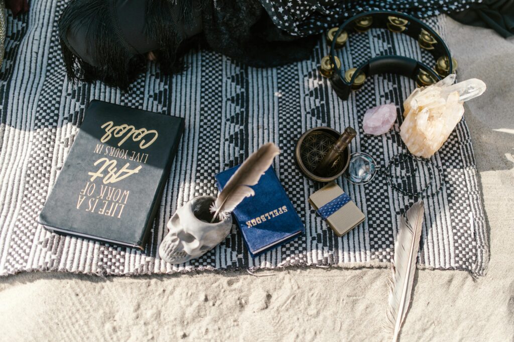 Flat lay of spiritual tools with crystals, skull cup, and feathers on a blanket outdoors.